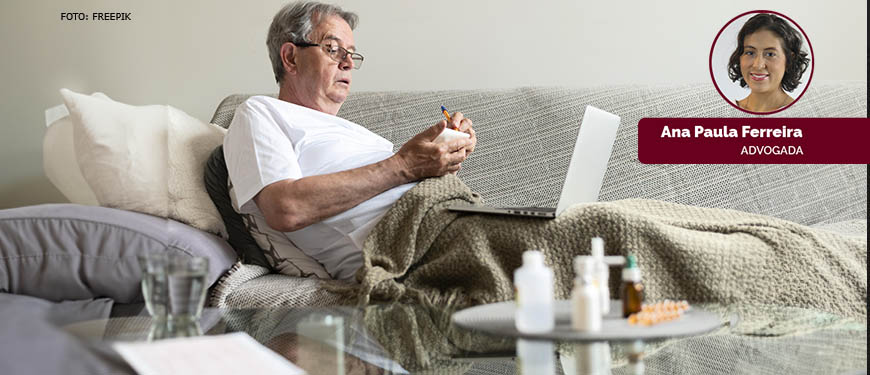 Fotografia mostra um idoso sentado em um sofá, de óculos e camisa branca, com um laptop no colo. Ele parece estar realizando alguma atividade no laptop.