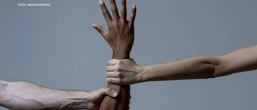 Imagem Acessível: Um braço negro levantado com a mão aberta para o alto é puxado por dois braços de pessoas brancas, como se impedissem o movimento da pessoa negra.
