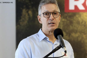 Romeu Zema, governador de Minas Gerais fala sobre um púlpito. Ele é um homem branco, grisalho de cabelos curtos e veste uma camisa azul clara.