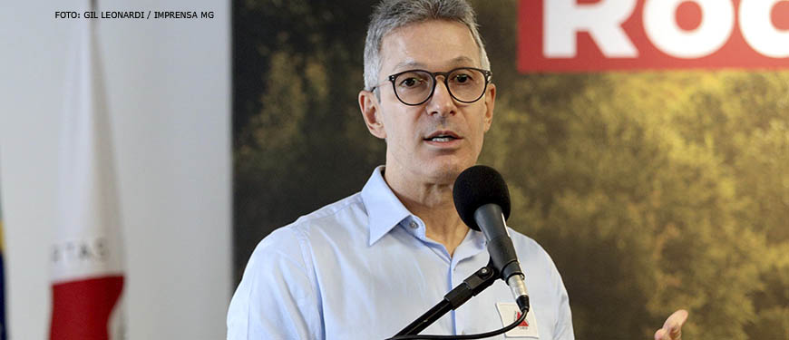 Romeu Zema, governador de Minas Gerais fala sobre um púlpito. Ele é um homem branco, grisalho de cabelos curtos e veste uma camisa azul clara.