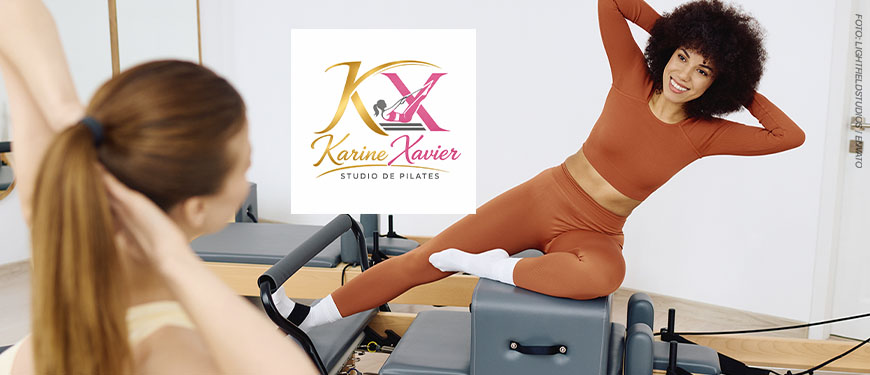 Imagem Acessível: Card de divulgação de convênio do SINJUS-MG com o Karine Xavier Studio de Pilates. A imagem mostra um estúdio de pilates com equipamentos . Em primeiro plano, desfocada à esquerda, aparece parte de uma pessoa sentada em um equipamento, observando a aula. Ao centro, está o logotipo do Karine Xavier Studio de Pilates. À direita, uma mulher negra, de cabelos cacheados volumosos, sorri enquanto realiza um exercício de alongamento lateral sobre um equipamento de pilates. Ela veste conjunto esportivo terracota de manga longa e calça legging, com meias brancas. Conteúdo textual: PILATES - Cuide do corpo e da mente com o novo convênio do SINJUS.