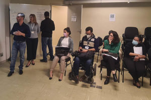 Representantes do SINJUS-MG, Alexandre Pires (Coordenador-geral) e Cristiane Sampaio (Coordenadora do Núcleo das Mulheres e Diretora Administrativa), apresentam slides aos servidores novatos durante o Serin 2022. Eles estão em pé lado a lado e falam para os ouvintes que estão sentados. Conteúdo textual: BOAS-VINDAS - SINJUS se apresenta aos novos servidores no Serin.