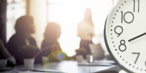 Arte com selo de “Urgente” no topo, informa no texto central que "sindicatos cobram nova reunião do GT de oito horas". A imagem mostra uma sala de reunião desfocada ao fundo e, em destaque, um relógio marcando as horas, simbolizando o tema da jornada de trabalho.