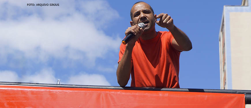 Homem negro de cabelos grisalhos (Wagner Ferreira) está sobre carro de som discursando com um microfone em sua mão.