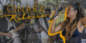 A imagem mostra a cantora Cinara Ribeiro em destaque, com microfone na mão e expressão vibrante durante uma apresentação. Ao fundo, sua banda toca ao ar livre em um ambiente descontraído. O texto informa que filiados ao SINJUS-MG têm 10% de desconto na contratação de shows da artista, por meio de um convênio exclusivo.