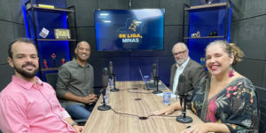 Imagem acessível: A imagem mostra o registo do episódio do podcast Se Liga, Minas, com quatro pessoas em um estúdio de gravação, sentadas ao redor de uma mesa com microfones. Ao fundo, uma TV exibe o logotipo do podcast. O texto em destaque informa: “Dirigentes do SINJUS debatem democracia e defesa dos servidores no Se Liga, Minas”.