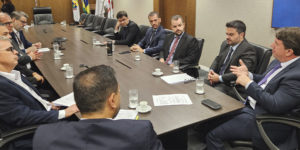 No card há dois registros fotográficos da Mesa de Negociações, as imagens mostram ângulos opostos de uma mesa de reunião em madeira escura, ao redor dela estão homens com trajes formais sentados. Sobre a mesa, copos d'água, xícaras de café e documentos. Ao fundo, uma televisão desligada e um quadro abstrato nas cores azul, amarelo e laranja. nesta reunião estão representantes da presidência do TJ, dirigentes sindicais do Serjusmig, Sindojus/MG, representando o SINJUS-MG estão o coordenador-geral, Felipe Rodrigues, o diretor administrativo, Alexandre Pires e o diretor de Finanças, Alex Aguiar.