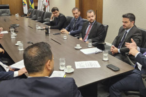 No card há dois registros fotográficos da Mesa de Negociações, as imagens mostram ângulos opostos de uma mesa de reunião em madeira escura, ao redor dela estão homens com trajes formais sentados. Sobre a mesa, copos d'água, xícaras de café e documentos. Ao fundo, uma televisão desligada e um quadro abstrato nas cores azul, amarelo e laranja. nesta reunião estão representantes da presidência do TJ, dirigentes sindicais do Serjusmig, Sindojus/MG, representando o SINJUS-MG estão o coordenador-geral, Felipe Rodrigues, o diretor administrativo, Alexandre Pires e o diretor de Finanças, Alex Aguiar.