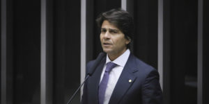 A imagem mostra o Deputado Pedro Paulo de terno falando ao microfone em um ambiente formal.