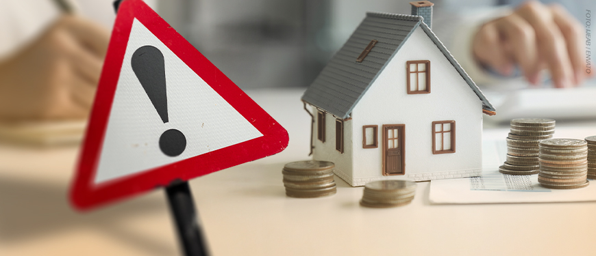 Imagem Acessível: A imagem mostra uma miniatura de casa cercada por moedas empilhadas, representando patrimônio e finanças pessoais. Em primeiro plano, um sinal de alerta vermelho com ponto de exclamação chama atenção para a necessidade de regularização. O texto reforça a orientação: “Saiba se você está na lista para regularizar a Declaração de Bens e Valores”, alertando os servidores sobre a obrigação anual de envio das informações patrimoniais. A arte tem tom informativo e preventivo, destacando a importância da atualização dentro do prazo. Na base da imagem, há a logomarca do SINJUS-MG.