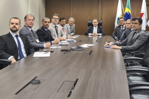 Foto de uma reunião formal com doze pessoas sentadas ao redor de uma mesa de conferência, com bandeiras ao fundo, estão presentes os representantes do Serjusmig, do SINDOJUS/MG, além do coordenador-geral do SINJUS, Alexandre Pires e Felipe Rodrigues, diretor de Assuntos Jurídicos do Sindicato. Na cabeceira da mesa, está o novo presidente do TJMG, desembargador Corrêa Junior,
