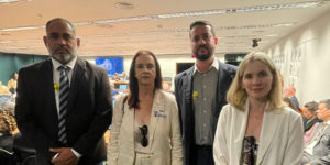 A imagem mostra quatro representantes sindicais posando lado a lado no centro do plenário da Câmara dos Deputados, durante uma audiência. Eles estão vestidos formalmente, com expressões sérias e engajadas. Ao fundo, é possível ver parlamentares e outros participantes sentados, além de uma tela com transmissão da audiência. O destaque da imagem é o texto: “Reforma Administrativa em foco: Fenajud e Sindicatos marcam presença em audiência na Câmara”.