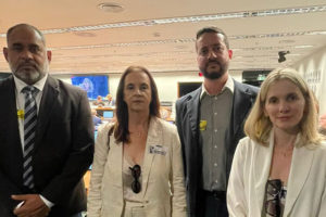 A imagem mostra quatro representantes sindicais posando lado a lado no centro do plenário da Câmara dos Deputados, durante uma audiência. Eles estão vestidos formalmente, com expressões sérias e engajadas. Ao fundo, é possível ver parlamentares e outros participantes sentados, além de uma tela com transmissão da audiência. O destaque da imagem é o texto: “Reforma Administrativa em foco: Fenajud e Sindicatos marcam presença em audiência na Câmara”.