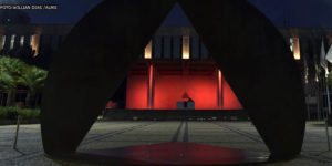 Vista noturna da ALMG (Palácio da Inconfidência), à frente do edifício, há uma escultura onde se vê um triângulo que remete à bandeira do estado de Minas. Pelo triângulo, pode-se ver o edifício iluminado em tons de vermelho. Conteúdo textual: Eleições 2022 - Na ALMG, ala progressista aumentou; no Congresso, cenário é obscuro.