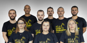 A imagem traz os integrantes da chapa 1 alinhados em um fundo neutro, vestindo camisetas com a frase “Só a luta te garante”, reforçando a identidade de mobilização e defesa da categoria. Estão na foto: Coordenação-Geral — Felipe Rodrigues e Rodrigues do Carmo; Diretoria Administrativa — Alexandre Paulo Pires da Silva; Diretoria de Acessibilidade e Inclusão — Wagner de Jesus Ferreira; Diretoria de Aposentados e Pensionistas — Janaína Torres Barbosa; Diretoria de Assuntos Jurídicos — Fellipe Rocha Tomanini Passaglio; Diretoria de Assuntos Sociais, Culturais e de Saúde — Patrícia Maria de Oliveira; Diretoria de Finanças — Alex Aguiar de Figueiredo; Diretoria de Formação e Política Sindical — Alexandre Furtado de Magalhães Gomes; Diretoria de Imprensa e Comunicação — Adriana Gonçalves Mota Teodoro