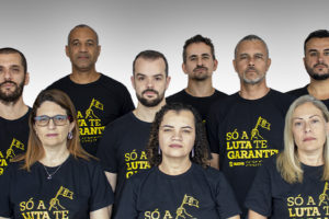 A imagem traz os integrantes da chapa 1 alinhados em um fundo neutro, vestindo camisetas com a frase “Só a luta te garante”, reforçando a identidade de mobilização e defesa da categoria. Estão na foto: Coordenação-Geral — Felipe Rodrigues e Rodrigues do Carmo; Diretoria Administrativa — Alexandre Paulo Pires da Silva; Diretoria de Acessibilidade e Inclusão — Wagner de Jesus Ferreira; Diretoria de Aposentados e Pensionistas — Janaína Torres Barbosa; Diretoria de Assuntos Jurídicos — Fellipe Rocha Tomanini Passaglio; Diretoria de Assuntos Sociais, Culturais e de Saúde — Patrícia Maria de Oliveira; Diretoria de Finanças — Alex Aguiar de Figueiredo; Diretoria de Formação e Política Sindical — Alexandre Furtado de Magalhães Gomes; Diretoria de Imprensa e Comunicação — Adriana Gonçalves Mota Teodoro