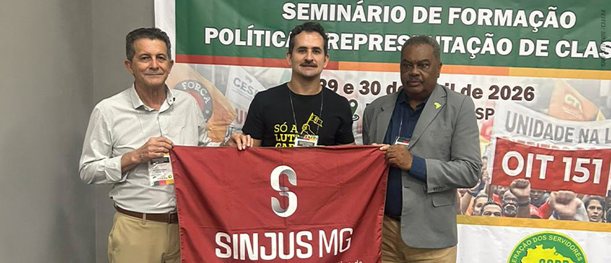 Imagem acessível: A imagem mostra o representante do SINJUS-MG segurando a bandeira do sindicato durante o Seminário de Formação Política e Representação de Classe, promovido pela CSPB, em ambiente interno com banner do evento ao fundo. No topo lê-se “Movimento nacional”. Na parte inferior o texto informa que o SINJUS participou do seminário e reforçou o debate sobre a atuação política dos sindicatos.