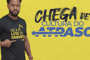 Arte de mobilização do SINJUS com fundo amarelo texturizado. À esquerda, homem negro, de cabelo curto e barba, veste camiseta preta com a frase “Só a luta te garante!” e aponta para a estampa. Ao centro, aparece o destaque “Chega de cultura do atraso”.Conteúdo textual: MOBILIZAÇÃO - SINJUS convoca categoria para acompanhar sessão do OE na próxima 4ªf.