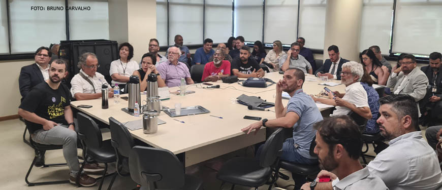 Foto de uma sala com uma ampla mesa em que, ao redor, estão sentados representantes de entidades sindicais, entre eles os dirigentes do SINJUS Alexandre Pires e Felipe Rodrigues.