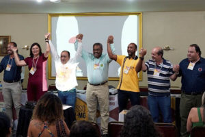 Representantes de entidades sindicais de servidores públicos municipais reunidos perante uma plateia, eles se dão as mãos e estão com os braços levantados; representando o SINJUS-MG estão o coordenador-geral, Alexandre Pires e o diretor de Assuntos Sociais, Culturais e de Saúde, Jonas Araújo.