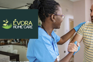 Imagem Acessível: A imagem mostra uma enfermeira atendendo um homem em sua casa, o auxiliando enquanto ele se levanta do sofá, ambos sorrindo. Sobre a imagem, aparece o texto: ‘Tenha atendimento médico domiciliar com o novo convênio do SINJUS’. No canto inferior esquerdo está o logo da empresa Évora Home Care.