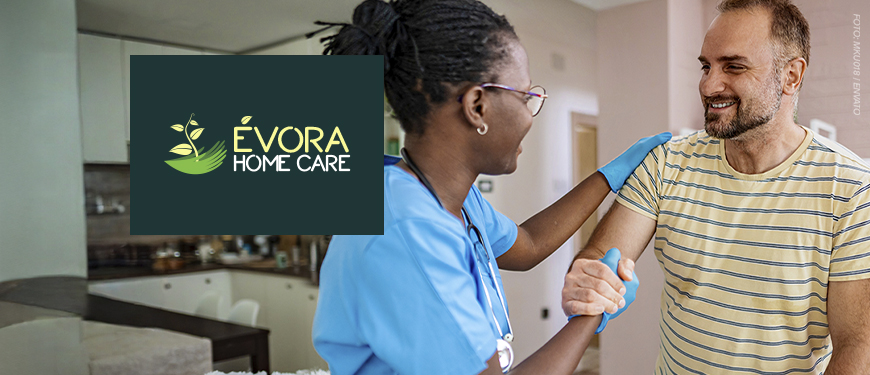 Imagem Acessível: A imagem mostra uma enfermeira atendendo um homem em sua casa, o auxiliando enquanto ele se levanta do sofá, ambos sorrindo. Sobre a imagem, aparece o texto: ‘Tenha atendimento médico domiciliar com o novo convênio do SINJUS’. No canto inferior esquerdo está o logo da empresa Évora Home Care.