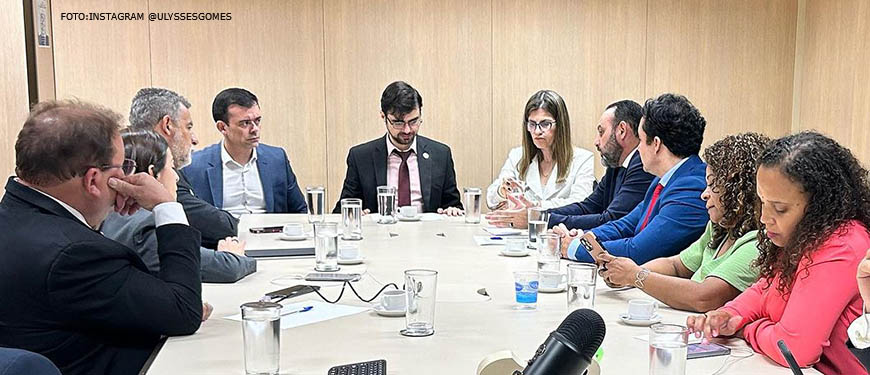 Imagem fotográfica de uma sala de reunião com uma mesa onde os participantes se encontram sentados com fisionomia de debater o assunto, acima da mesa se vê papéis e um microfone. Estão na foto deputados estaduais mineiros e representantes do Ministério da Fazenda.