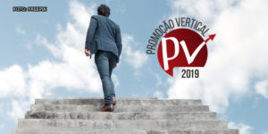 Homem de terno azul subindo uma escada que avança para o alto, rumo ao céu. Ao lado está uma arte relativa à Promoção Vertical 2019.