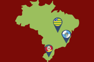 Imagem do mapa do Brasil no tom de verde, com um fundo vermelho escuro, no mapa há o destaque dos estados Goiás, Rio de Janeiro e Rio Grande do sul, representados pelas suas respectivas bandeiras, em um ícone de localização na cor azul.