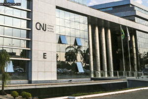 Vista frontal da Sede do Conselho Nacional de Justiça, um edifício com pilares revestidos em granito e vidros espelhados.