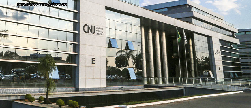 Vista frontal da Sede do Conselho Nacional de Justiça, um edifício com pilares revestidos em granito e vidros espelhados.
