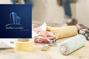 Imagem acessível: A imagem mostra uma mesa com ferramentas de construção, como rolo de pintura, fita adesiva e furadeira, com pessoas trabalhando ao fundo desfocado. O texto informa: “Garanta descontos em reformas e construções civis com o novo convênio do SINJUS”. Também aparece o logotipo da empresa Mellká Carvalho Reformas.