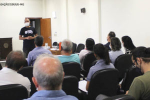 Foto de um auditório com diversos servidores assentados ouvindo o Wagner Ferreira, diretor de Assuntos Jurídicos SINJUS-MG (homem negro, com cabelo bem curto, usa camisa preta e máscara).