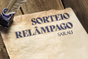 Imagem Acessível: A imagem apresenta um convite visual para um "Sorteio Relâmpago" relacionado a um sarau com participação da filiada do SINJUS-MG. Em destaque, há uma folha de papel envelhecido sobre uma mesa de madeira rústica, com um tinteiro azul-escuro e uma pena repousando sobre ela — remetendo à escrita clássica. No papel, lê-se em letras grandes: “SORTEIO RELÂMPAGO - SARAU”, seguido do tema “A tirania do gozo imediato x A última dor que me salvou”. Abaixo, há informações práticas: inscrições até o dia 8 de maio (quinta-feira), resultado no dia 9 (sexta-feira), e datas dos eventos — 10 de maio (sábado) às 20h e 11 de maio (domingo) às 19h, no Teatro da Biblioteca Pública Estadual de Minas Gerais. A marca do SINJUS-MG aparece na parte inferior da imagem. O visual retrata um evento cultural com atmosfera reflexiva e artística.