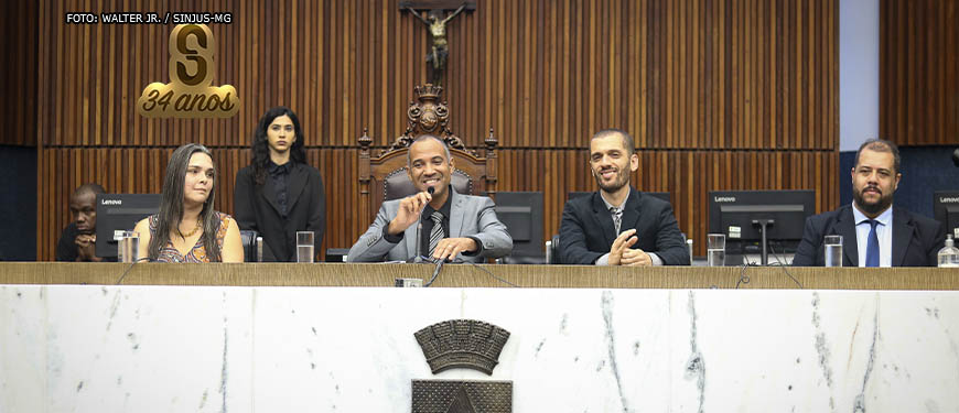 Mesa diretiva do Plenário da Câmara Municipal de Belo Horizonte, compõem a mesa Flávia da Silveira, representando os membros do Conselho Fiscal do Sindicato, Wagner Ferreira, vereador e diretor de Assuntos Jurídicos e presidindo a mesa, Alexandre Pires, coordenador-geral e Sérgio Martins, gerente administrativo representando os funcionários do Sindicato. Conteúdo textual: 34 ANOS - ATUAÇÃO DO SINJUS É HOMENAGEADA EM NOITE ESPECIAL NA CÂMARA DE BH.