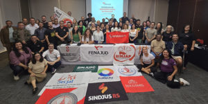 A imagem mostra um grande grupo de dirigentes sindicais reunidos em uma sala, posando para a foto atrás de várias bandeiras de sindicatos de diferentes estados.