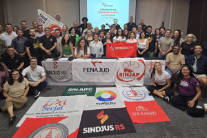 A imagem mostra um grande grupo de dirigentes sindicais reunidos em uma sala, posando para a foto atrás de várias bandeiras de sindicatos de diferentes estados.
