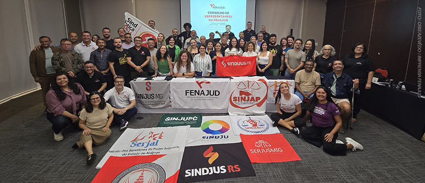 A imagem mostra um grande grupo de dirigentes sindicais reunidos em uma sala, posando para a foto atrás de várias bandeiras de sindicatos de diferentes estados.