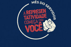 Imagem Acessível: Fundo azul-escuro, com composição gráfica em vermelho e branco com a frase "Mês do Servidor - A representatividade começa com você”, acompanhada de uma ilustração de um dedo apontando para a frente. Conteúdo textual: Valorização - SINJUS promove campanha e sorteio especial em celebração ao Mês do Servidor.