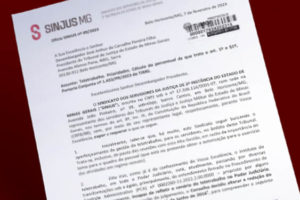 Montagem digital de uma página de um ofício protocolado do SINJUS-MG sobre fundo vermelho escuro. O documento está em um papel timbrado do Sindicato.