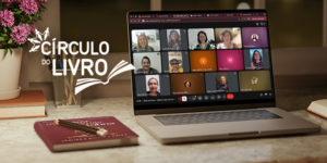 Imagem acessível: A imagem mostra um ambiente aconchegante de estudo e leitura, com luminária, flores e um notebook sobre a mesa exibindo uma reunião virtual com várias mulheres participantes. No topo lê-se “Protagonismo feminino”. O texto principal informa: “NM se reúne para discutir o poder da intuição feminina no Círculo do Livro”. Ao lado aparece o logotipo do projeto Círculo do Livro, indicando o encontro promovido pelo Núcleo das Mulheres do SINJUS-MG para debate e troca de reflexões.