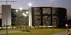 Vista da Cidade Administrativa ao entardecer, dois edifícios curvos, revestidos com vidros escuros em toda a fachada.
