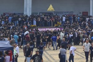 A imagem mostra uma grande multidão de pessoas reunidas na prça em frente à sede da Assembleia Legislativa de Minas Gerais em uma manifestação. A multidão é diversa, com indivíduos de diferentes idades e aparências protestando contra o RRF.