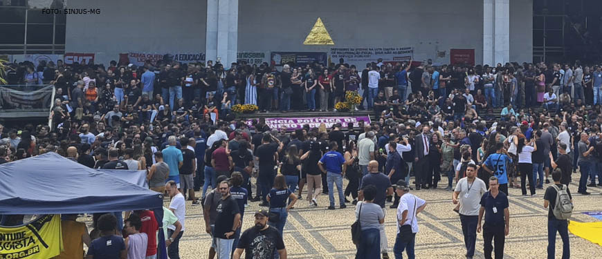 A imagem mostra uma grande multidão de pessoas reunidas na prça em frente à sede da Assembleia Legislativa de Minas Gerais em uma manifestação. A multidão é diversa, com indivíduos de diferentes idades e aparências protestando contra o RRF.