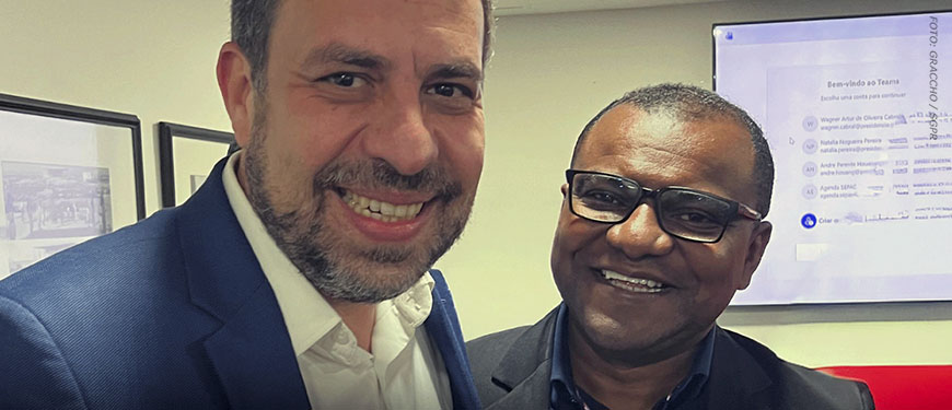 Foto de duas pessoas sorrindo, o ministro da Secretaria Geral da República, Guilherme Boulos e o coordenador-geral da Fenajud, Janivaldo Ribeiro. em ambiente interno, com uma tela ao fundo.