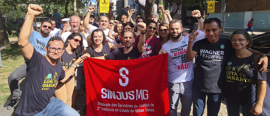 Fotografia com servidores e filiados na luta contra o RRF, na imagem se vê os mesmo com punhos erguidos e a bandeira do SINJUS na cor vermelha.