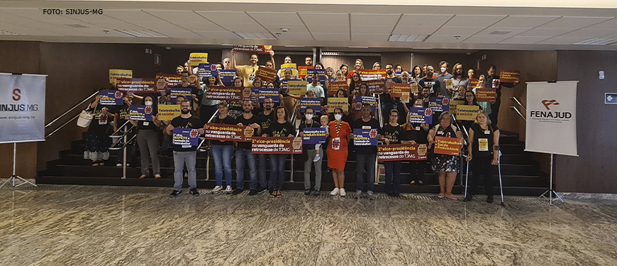 Grupo numeroso de servidores está reunido na escadaria do hall da sede do TJMG, no grupo há mulheres, homens e um bebê de colo acompanhado da mãe. Eles portam cartazes e faixas com palavras de ordem a favor do Teletrabalho.