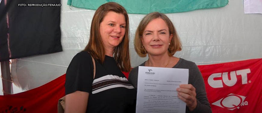 Imagem Acessível: Arlete Rogoginski, coordenadora-geral da Fenajud, mulher branca de cabelos e olhos castanhos entregwa documento para a presidenta do Partido dos Trabalhadores (PT), Gleisi Hoffmann, mulher branca de cabelos loiros e olhos azuis.