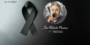 À esquerda há uma fita preta em sinal de luto, ao lado da fita está a foto de um homem negro com cabelos grisalhos e crespos falando ao microfone, abaixo dele está seu nome José Roberto Pereira, acompanhado da data de seu falecimento 7/8/2022.