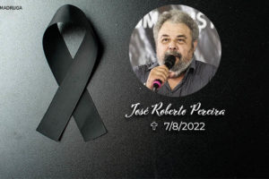 À esquerda há uma fita preta em sinal de luto, ao lado da fita está a foto de um homem negro com cabelos grisalhos e crespos falando ao microfone, abaixo dele está seu nome José Roberto Pereira, acompanhado da data de seu falecimento 7/8/2022.